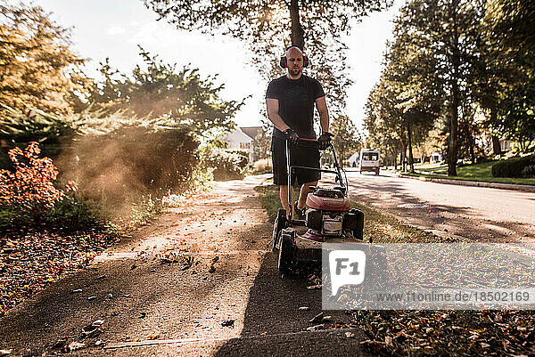 Front view of man mowing grass along sidewalk