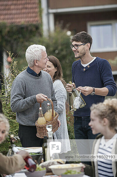 Father and son holding bottles of white wine and apple juice and talking at farmhouse  Bavaria  Germany