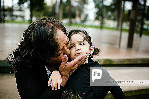 Grandmother kissing granddaughter while sitting in park