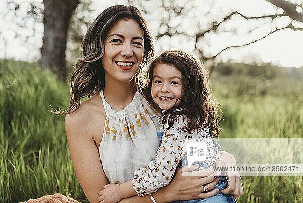 Portrait of mother and daughter in backlit field smiling at camera