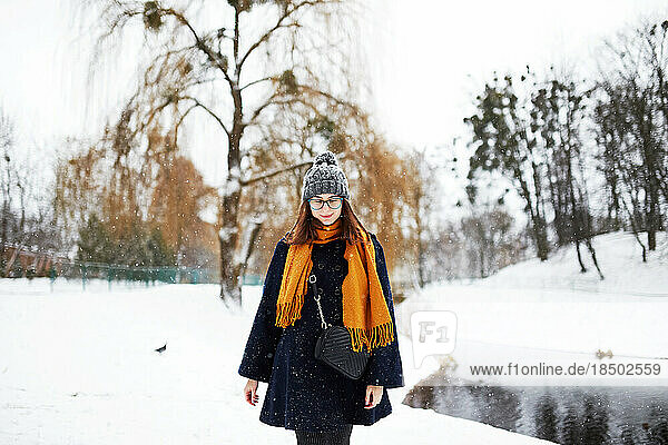 woman in a yellow scarf and a blue coat walks alone in a snowy park