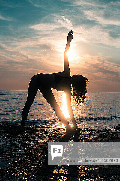 Young woman doing yoga at sunset beach