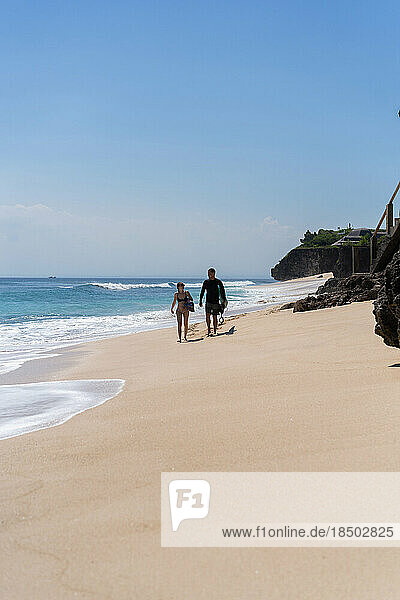 Young couple of surfers with surfboards walk along the ocean.