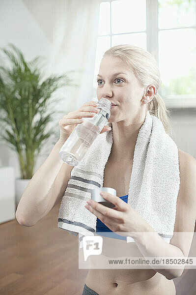 Young woman drinking water after exercise at living room  Bavaria  Germany