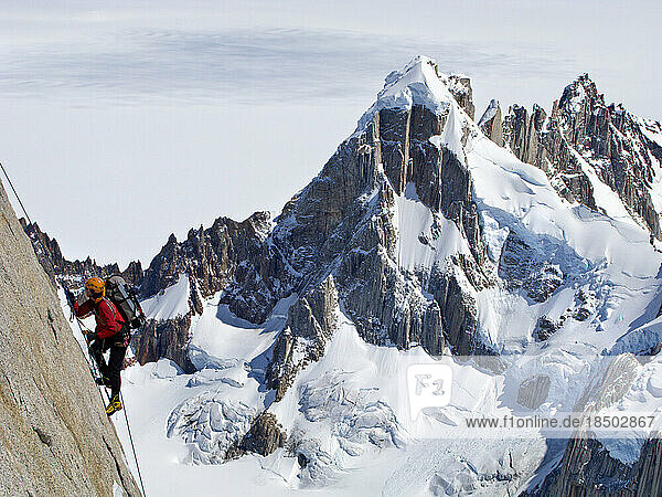 A climber climbs the steep north face of Torre Egger  with the peaks of Cerro Rincon and the glaciers of the Southern Patagonia