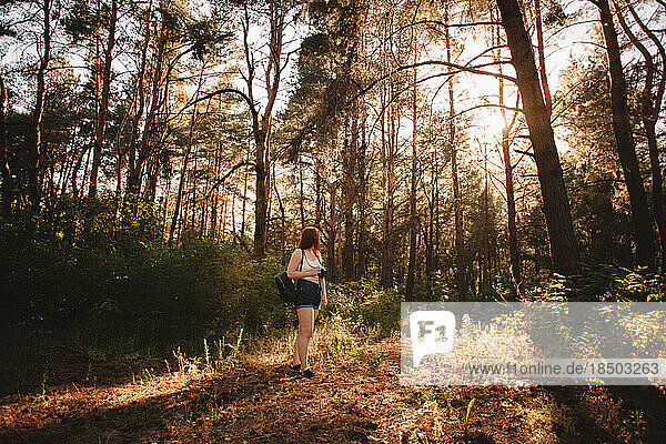 Female hiker with camera walking in forest during summer