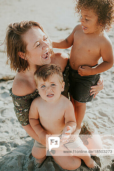 Laughing mother holding twin toddler boys in the sand