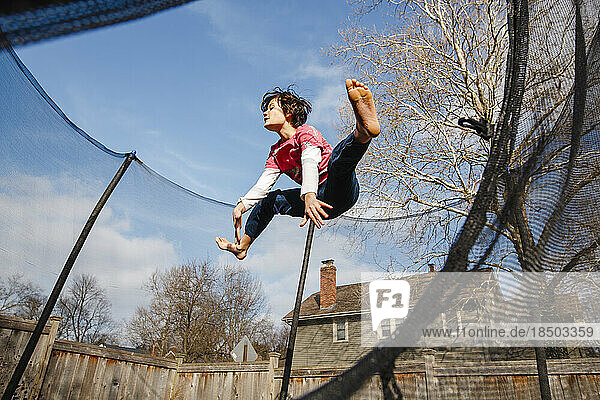 A happy boy does split jump on trampoline outside