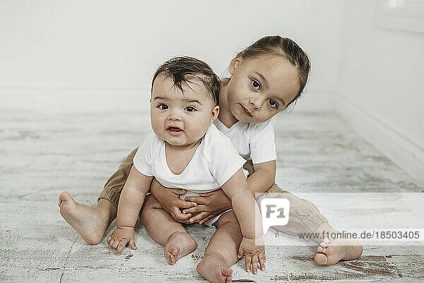 Portrait of toddler boy and baby girl sitting on white floor
