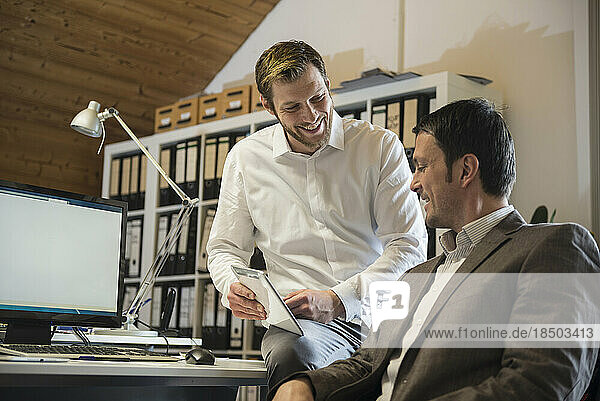 Two businessmen using digital tablet in an office and smiling  Bavaria  Germany