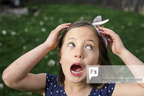 A small girl on a breezy day holds a flower blossom on head as a hat