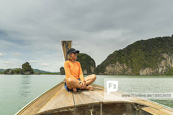 Woman smiling sitting in typical Thai boat admiring mountain landscape