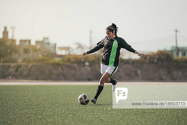 Young female soccer player kicking ball.