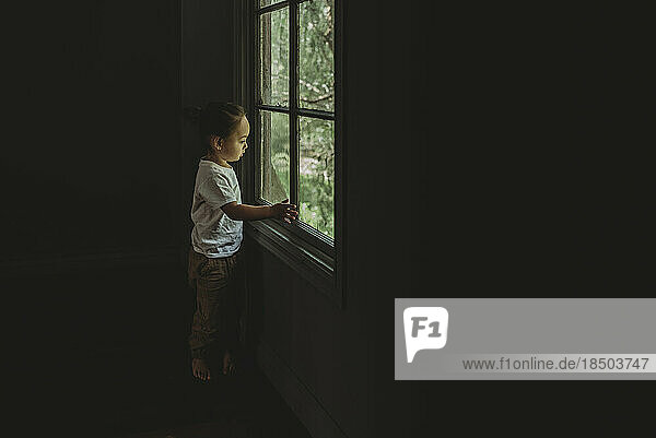 Preschool aged boy looking out the window at the trees