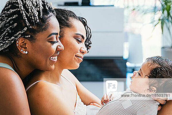 Side view of smiling lesbians playing with cute baby boy at home