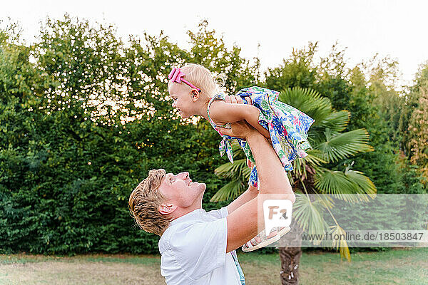 Dad throws his baby girl in his arms in the summer outdoors