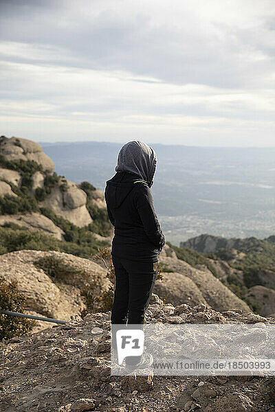 Girl from behind with hood observing the mountain landscape