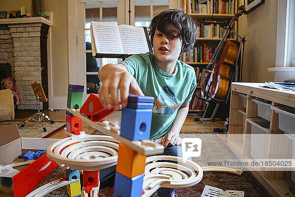 A boy sits in living room building wooden marble run