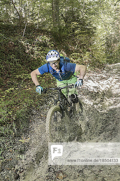 Mountain biker riding through puddle and splashing water in forest
