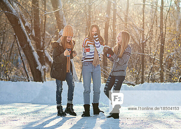 Three tween girls drinking coffee in the snow on winter day.