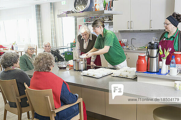Nurse preparing food with senior inhabitants in rest home