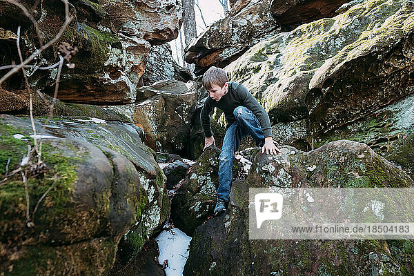 Boy scrambling over rocks on hike in forest