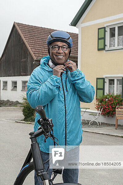 Senior man fastening on bicycle helmet and smiling  Bavaria  Germany