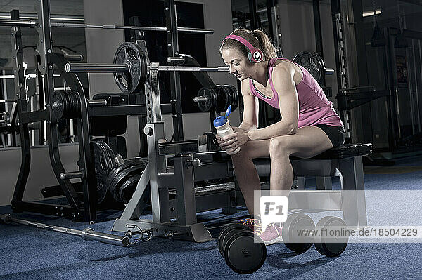 Mid adult woman taking a break after exercising and listening to music in the gym  Bavaria  Germany