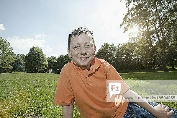 Boy smiling and sitting on a field in park  Munich  Bavaria  Germany