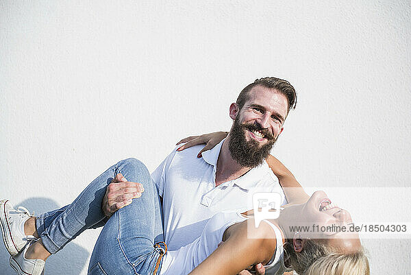 Happy young man carrying woman in front of wall  Bavaria  Germany