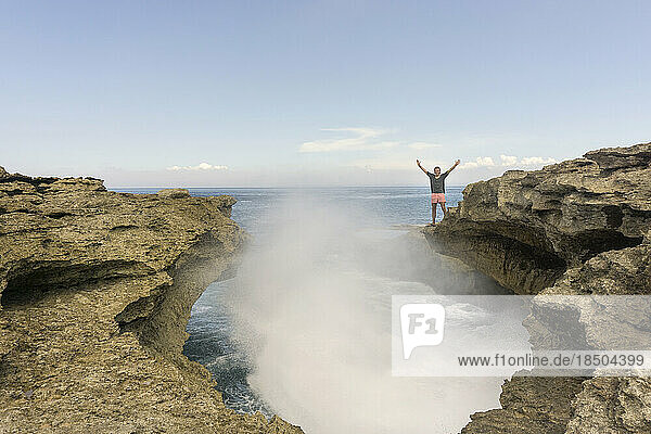Young man standing on rock formation by splashed sea waves  Nusa Lembongang  Bali  Indonesia