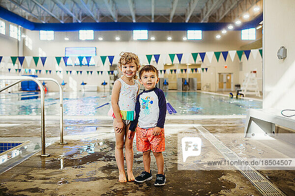 Young boy and girl smiling at indoor gym pool wearing swim suits