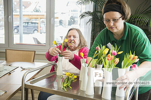 Caretaker and senior woman arranging flowers and vases at rest home