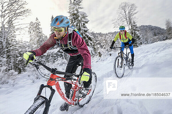 Mountain bikers in sportswear riding cycle in snow