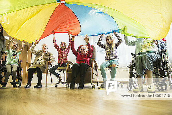 Girls and senior women doing gentle sports exercise with parachute in rest home