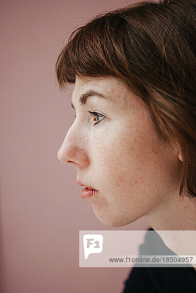 profile of a freckled woman on a pink background