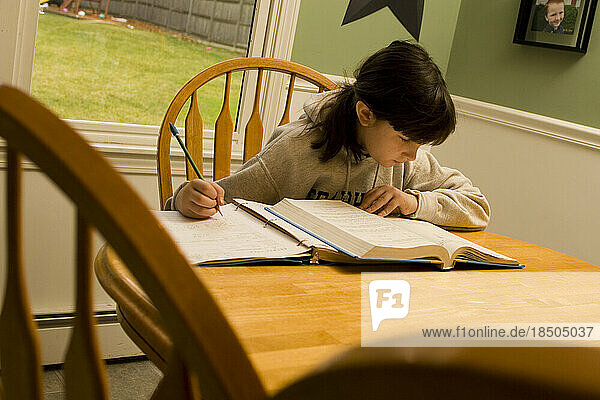 A ten-year-old girl sits at her kitchen table doing her homework on a weekend afternoon.