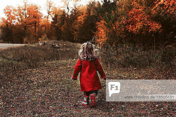 Child walking outside wearing red coat on a beautiful fall day
