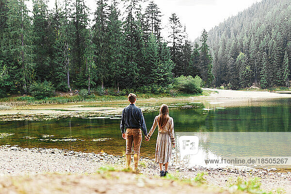 man and woman holding hands near a forest lake