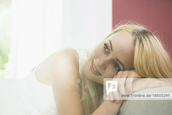 Thoughtful beautiful young woman relaxing on sofa in the living room  Munich  Bavaria  Germany