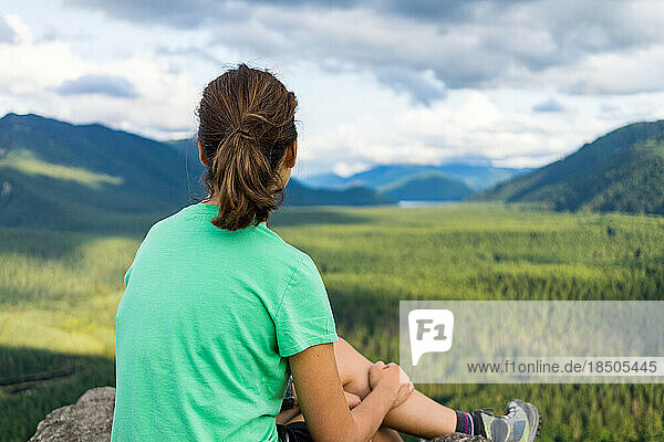 Hiker girl looking at green hills and lake from the edge in Washington