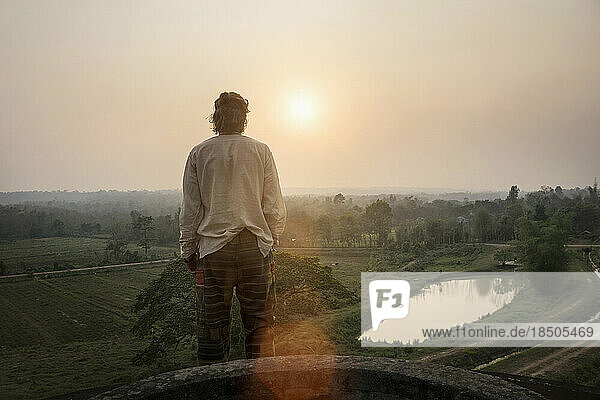 Rear view of a young man standing on mountain and looking at view during sunset  Laos