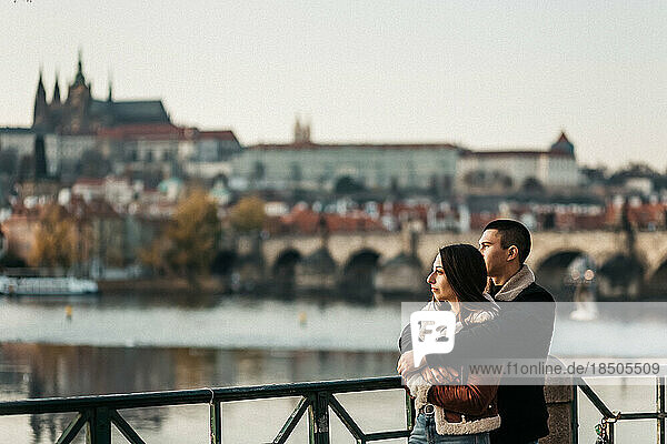 man and woman hugging near river and bridge in center of Prague