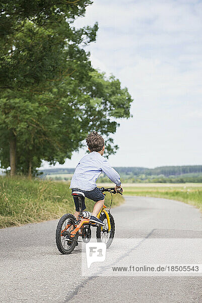 Rear view of a child riding bicycle on road in the countryside  Bavaria  Germany