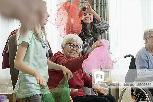 Girls with senior woman doing gentle sports exercise with cloth in rest home