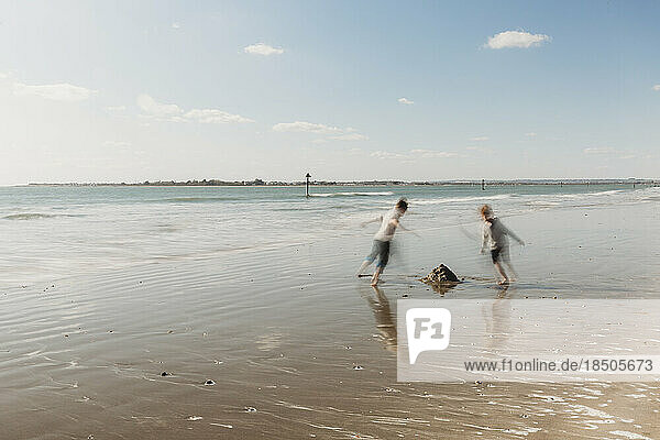 Two children running on beach against blue sky