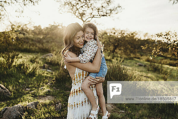 Beautiful mother holding young daughter in bright grassland