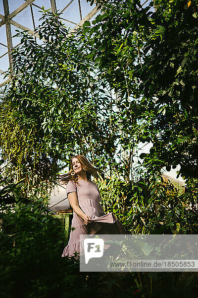Woman twirls dress in botanic setting with tropical plants