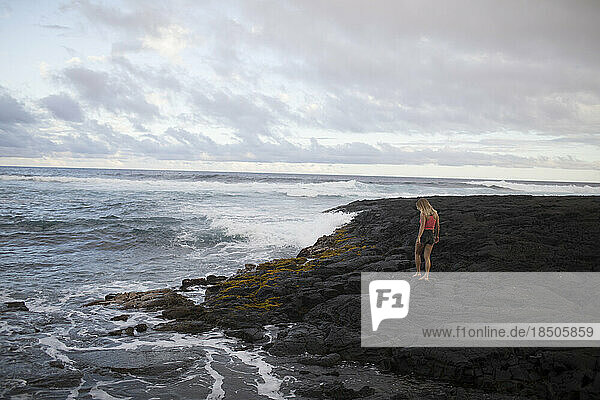 A girl is walking on lava rocks near the ocean  Big Island  Hawaii.