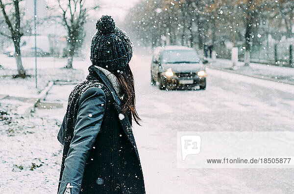 woman in black is walking through a snowstorm on a snowy road